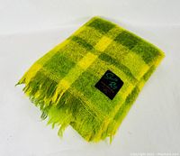 Folded fluorescent green and yellow plaid wool sports rug with fringed edges, showing the 'Sports Rug Eaton's' label.