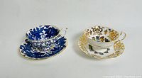 Two vintage tea cup and saucer sets side by side, one cobalt blue leaf motif and one Canada coat of arms with gold highlights