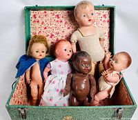 Five old dolls arranged inside an open vintage green toy chest showing their size, condition and appearance.