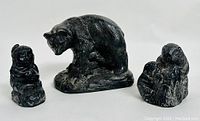 Three black sculptures side by side: child figurine, standing bear, and beaver family.