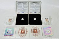 Front view of two Canada Post Millenium stamp and coin sets showing the quarter dollar coins centered on black velvet, three unused stamps per set with holographic backgrounds below, accompanied by official documentation in silver metal cases.