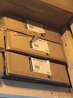 Three stacked sealed boxes labeled SpeakerCraft AccuTuneBox 10 in a garage rafter location.