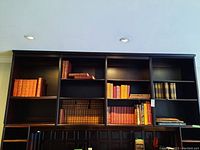 Bookshelves with leather-bound and cloth-bound books of varied colors including several orange and red volumes on the upper and middle shelves.