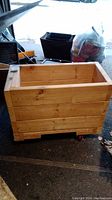 View of the outside of the rectangular wooden box showing horizontal wooden planks and red caster wheels underneath.