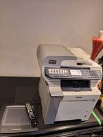 Brother MFC-9840CDW wireless printer with keypad and display, Monoprice tablet and Samsung remote beside it