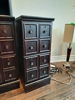 Front view of one of the dark wood side cabinets showing 8 drawers with round knobs and keyholes.