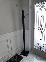 Full height view of the black wooden coat rack positioned in a corner with a decorative glass door beside it.