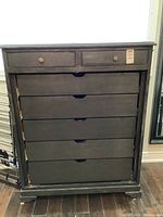 Full front view of the seven drawer black dresser, showing two smaller top drawers with brass knobs and five larger drawers below with recessed curved pulls. Doors removed revealing inside.
