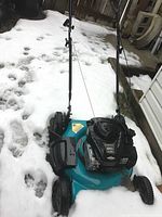 Photo showing the full lawn mower on snowy ground, highlighting the blue deck and black engine.
