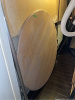 Full view of round maple table top leaning against a wall, showing overall shape and finish.