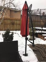 Full view of red cantilever umbrella closed, showing frame and base in snowy backyard