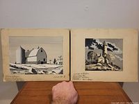 Both small black and white paintings side by side showing country and barn scenes, with some water staining visible on boards.
