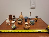 Photo showing all 11 miniature vases arranged on a wooden surface with measuring tape showing about 12 inch length of display area