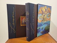 Two hardcover books and slipcase, showing the front covers and spines, displayed on a wooden surface.