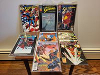 Eight comics sealed in plastic sleeves on boards laid out on a dark wood table. Shows full set including Superman (three issues), Spawn Todd's Toys, two Hawkman issues, Terror Inc., Return of New Gods.