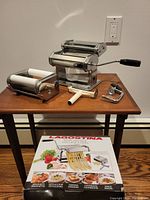 Full view of Lagostina pasta machine with attachments and box arranged on a wooden table against wall with power outlet