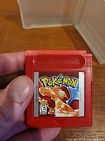Close-up of the red Pokemon Red Gameboy cartridge held in a hand showing label with Charizard and Pokemon text.