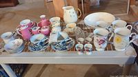 Wide view of assorted Belleek and Blue Danube porcelain items including cups, saucers, pitchers, and small bowls and creamers on a cart.