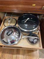 Drawer containing large, medium, and small stainless steel pots with glass lids, and a stainless steel steamer insert