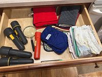 Top view of kitchen drawer containing flashlights, magnifying glass, pot holders, and kitchen towels.