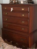 Front view of a Drexel wooden chest of drawers with five drawers and brass pull handles, standing on curved legs with a scalloped base.