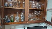 Glassware in wooden cabinet shelves including various glasses, colorful bases, and tumblers with text