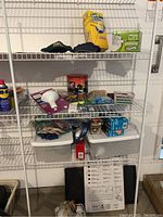 Shelf containing various household cleaning items, lightbulbs, spray can, gloves, small boxes, and a white boot tray