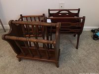 Three wooden magazine stands with various spindle and carved designs shown together on carpeted floor.