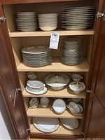Wide view inside cabinet showing multiple stacks of various plates, bowls, cups, and serving pieces with floral and gold pattern.
