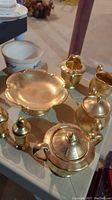 Gold tone tea set items including salt and pepper shakers, dessert plate, creamer and sugar bowl with teapot, all with ornate engraved designs.