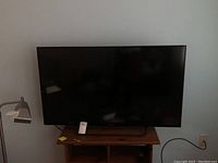 Front view of Sony TV placed on wooden stand showing screen and surrounding area including a lamp and power outlet.