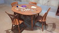 Full view of round wooden table with four chairs displayed surrounding it. Various small items are spread on table surface.