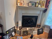 Wide photo showing multiple framed wall art pieces around fireplace and on mantel including black and white photos, watercolors, and other framed art in classic and natural wood frames.