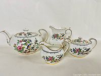 Full view showing the teapot, cream jug, sugar bowl with lid, and milk jug with floral and gold trim detail, arranged in a line.