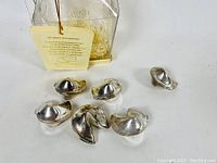 Six silver plated fortune cookie replicas displayed outside the original container along with the original string tag.