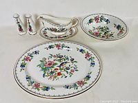 Photo showing the set consisting of salt and pepper shakers, gravy boat with underplate, serving bowl, and serving plate in floral pattern with gold trim.
