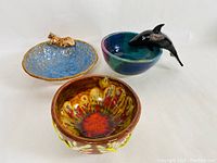 Photo showing three pottery bowls: one with a leopard figure, one with a dolphin figure, and one multicolored with yellow decoration.