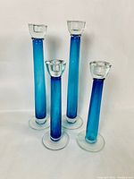 Front view of the set of 4 royal blue and clear blown glass long stem candle holders of varying heights, standing upright.