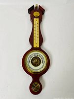 Front view of vintage wooden and brass wall-mounted analog barometer with integrated thermometer.