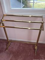 Front view of brass comforter rack placed on carpet in front of window