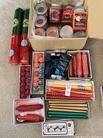 Large group of boxed and unboxed new candles including various colored wax tapers and tealights, boxed drip guards, and glass jar candles.
