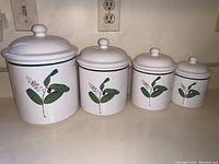 Front view of all four white ceramic canisters with floral and green trim design.