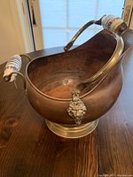 Side angle of copper coal scuttle showing lion head detail and Delft porcelain handle