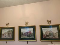 Three professionally framed and matted watercolor prints hung on wall with brass accent bows mounted above frames, depicting Shaw Festival theatres.