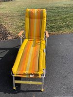 Front view of the vintage lounge chair with yellow-orange striped cushion and wooden armrests on metal frame.