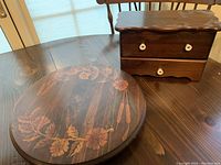 Photo of wooden turntable with inlaid floral and cattail design on round surface and apothecary cabinet showing drawer and hinged lid with white knobs.