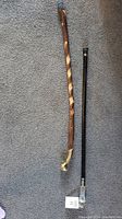 Two canes side by side on carpet. One wooden spiral cane with gold-colored curved handle, one slim black cane.