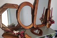 Four mirrors and two wooden wall mount candle holders with floral candle decoration arranged together on a shelf.