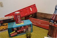 Lot overview showing red plastic crate, wooden crate, boxed model truck, sealed hot rod model, Coca Cola can, and glass.