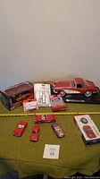 Wide view of 11 Corvette collectible model cars mostly in red, some packaged, arranged on green tablecloth with measuring tape.